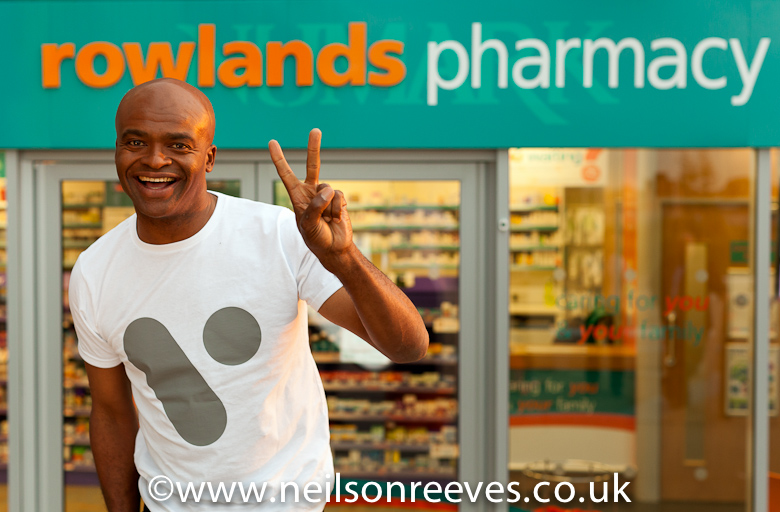 kriss akabusi smiling doing the V for victory sign outside rowlands pharmacy for national advertising campaign for V healthcare systems