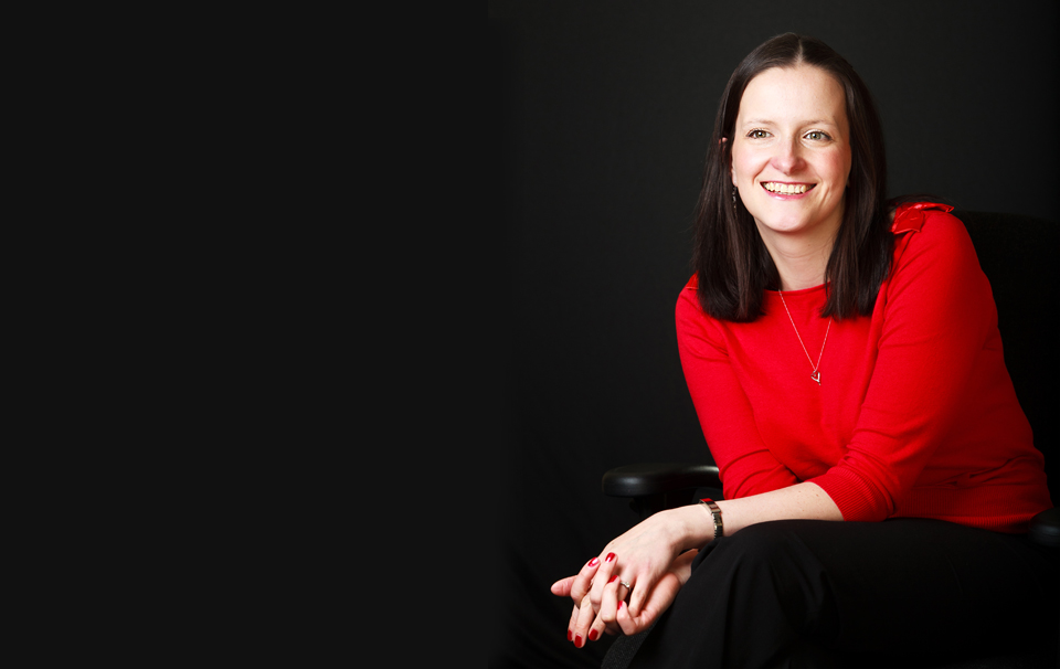 corporate portrait of a lady wearing red jumper shot against a black background