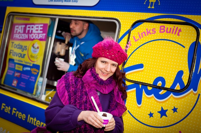 Lady smiling as she takes an ice cream from an ice cream van in the distance