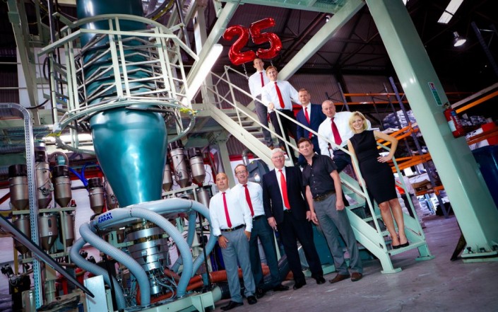 people stood in a v shape next to huge plastic bag manufacturing machine