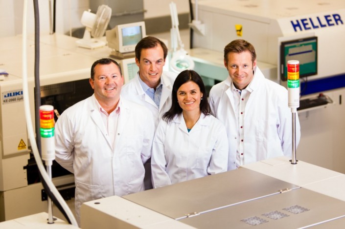 People in Doctor White Coats stood around a machine that makes printed circuit boards