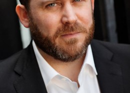 Actor headshot featuring tom Aldersley wearing a black suit no tie