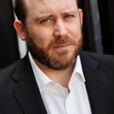 Actor headshot featuring tom Aldersley wearing a black suit no tie