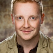 Actor headshot on brown speckled background featuring male with red hair