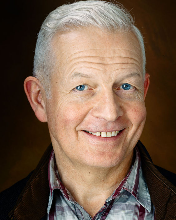 Mature businessman man with grey hair smiling, brown jacket, check shirt, brown background