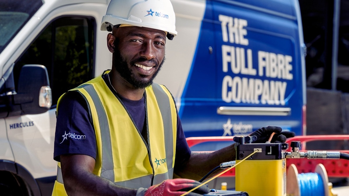 Black telcom engineer full PPE smiling at camera with Telcom van behind