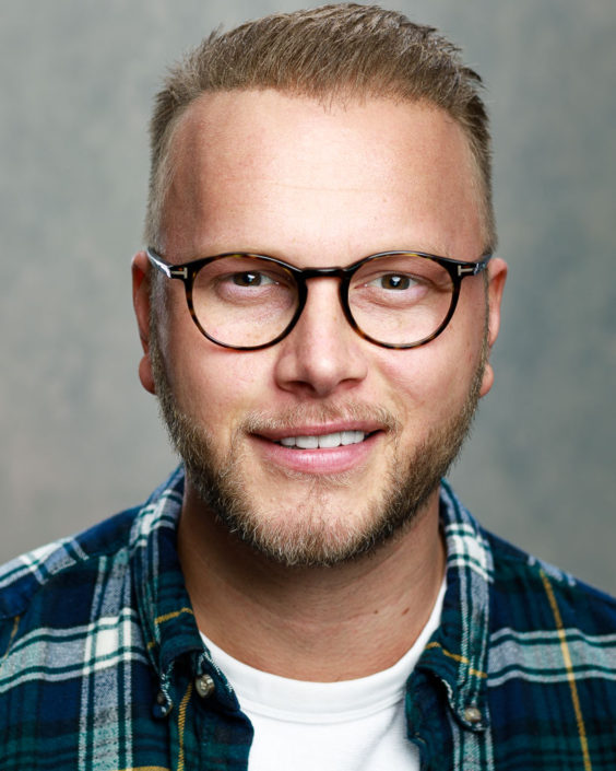 young designer wearing glasses smiling short spikey hair green check shirt with white t shirt underneath