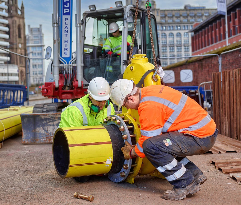 construction worker putting collar on gas main liver buildings behind