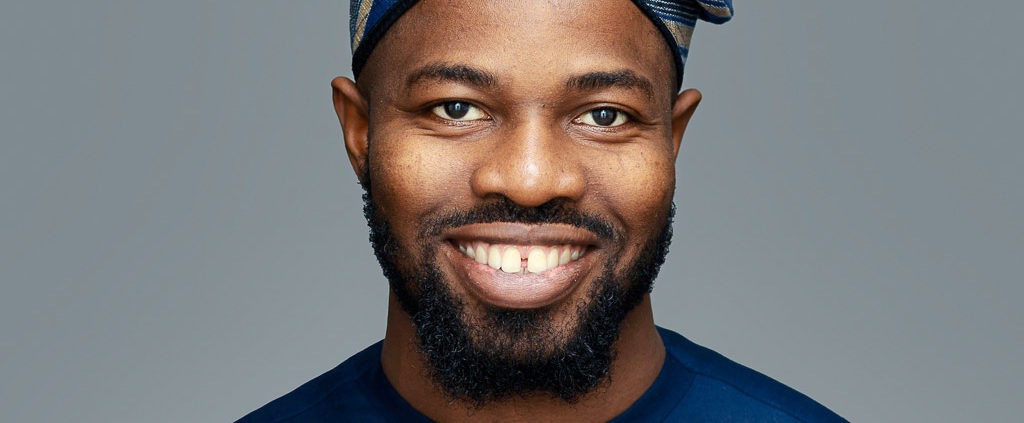 corporate headshot grey background featuring a black man wearing an African dress and hat