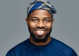 corporate headshot grey background featuring a black man wearing an African dress and hat