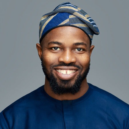 corporate headshot grey background featuring a black man wearing an African dress and hat