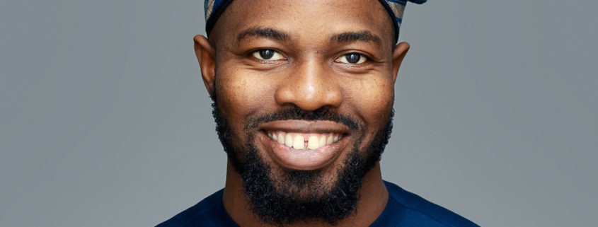 corporate headshot grey background featuring a black man wearing an African dress and hat