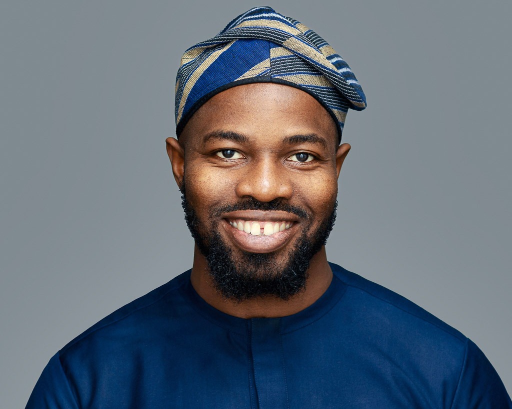 corporate headshot grey background featuring a black man wearing an African dress and hat