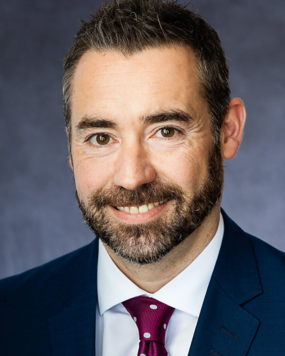 Middle aged business man smiling, white shirt, blue jacket and grey speckle background