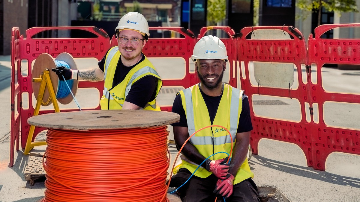 Black and white engieers happy installing fibre optic cable into manhole