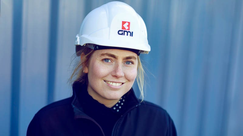 young female site manager wearing hard hat shot in front of grey construction site hoardings 