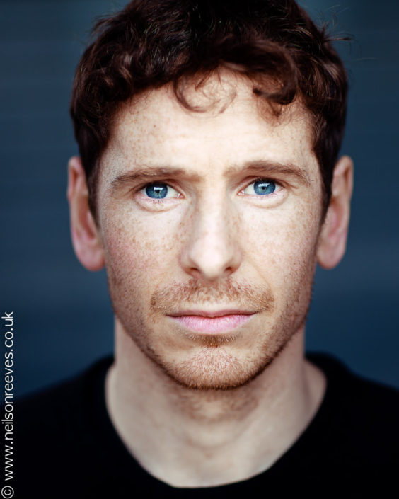 close crop actor headshot featuring actor Gerard kearns with freckles and stunning blue eyes and grey background