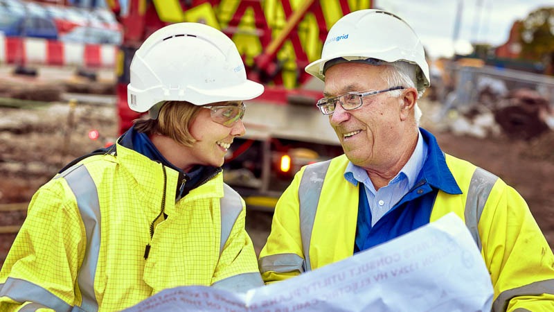 Female site manager in full PPE looking at plans with mature male construction worker in PPE