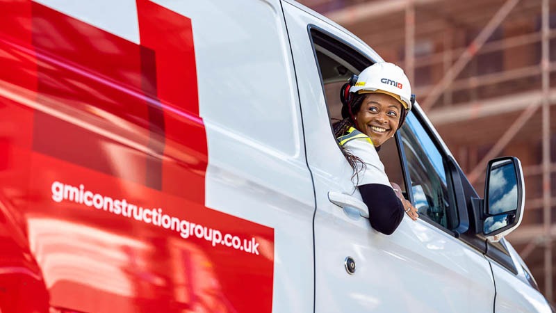 Black female construction worker reverses GMI construction van wearing hard hat and PPE