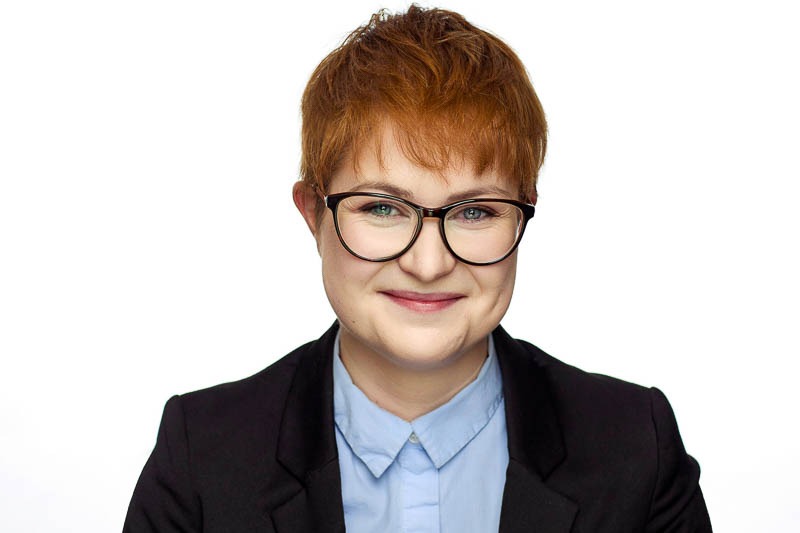 corporate headshot white background featuring a young woman with short red hair wearing glasses